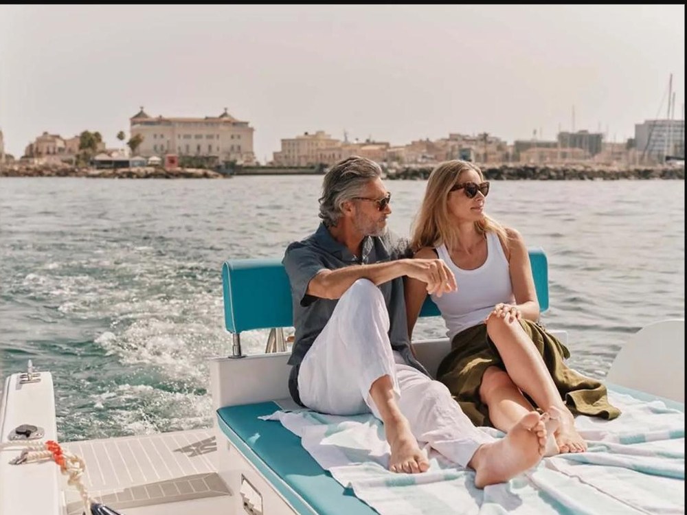 A couple relaxes on the deck of a private yacht tender with a Mediterranean harbor town in view