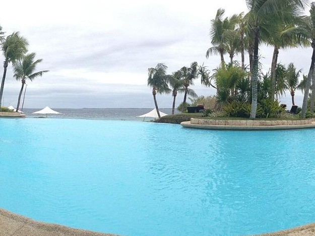 A resort infinity pool framed by palm trees overlooking the sea