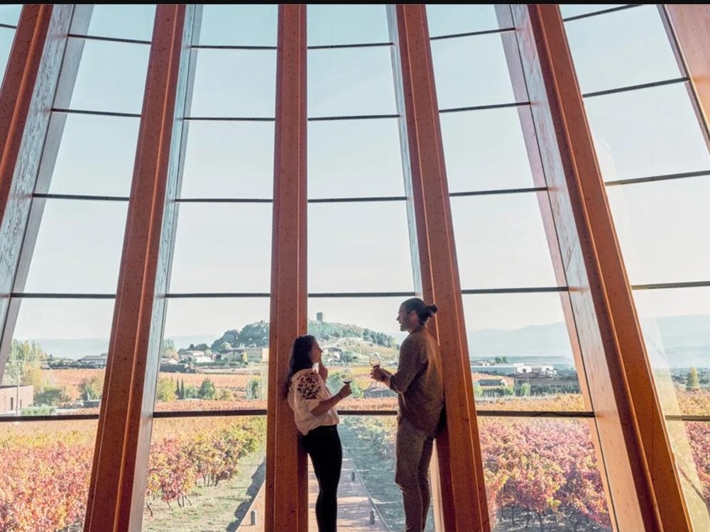 A couple shares wine with vineyard views from a glass-walled tasting room at Bodegas Ysios in Spain's Rioja region